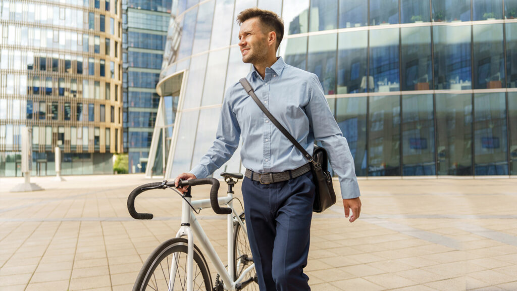 Ein lächelnder Geschäftsmann schiebt sein Fahrrad.