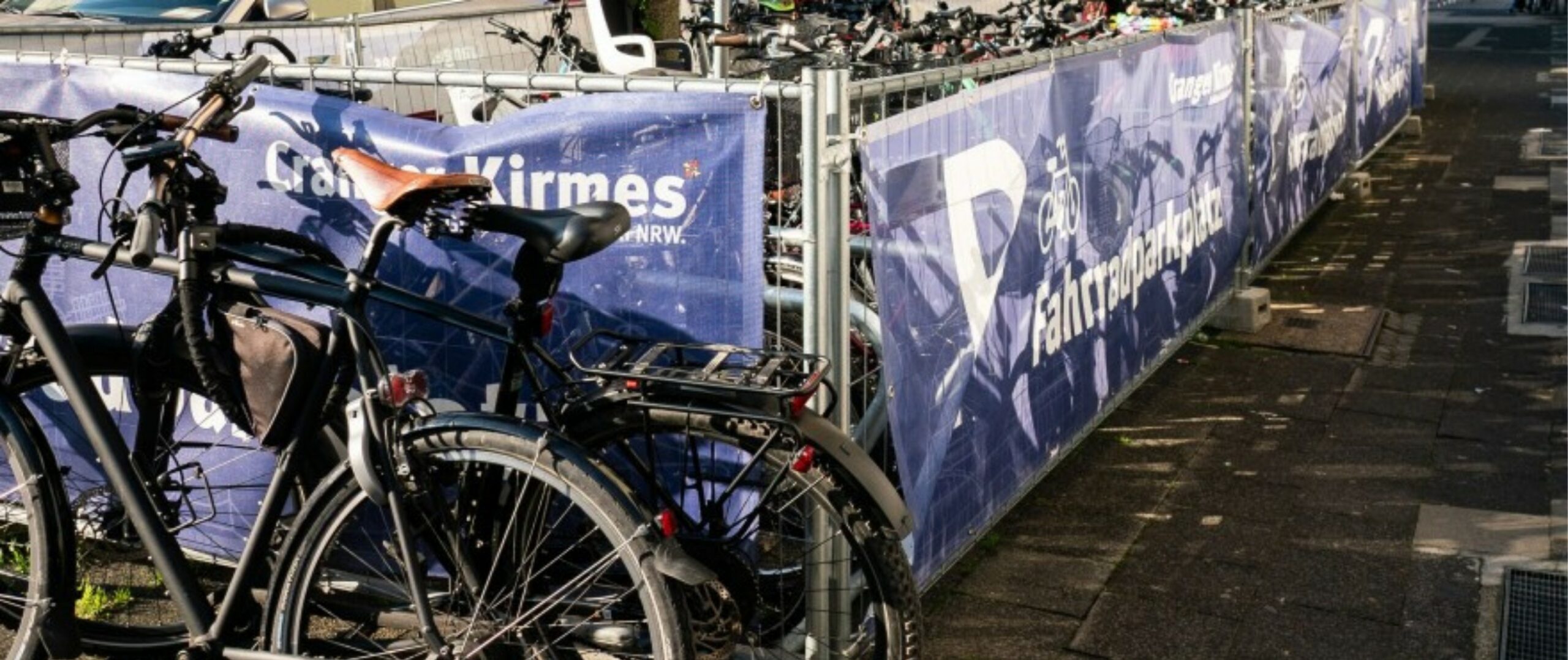 Fahrräder sind in einem Bereich abgestellt, umrandet von einem Zaun mit dem Motiv "Cranger Kirmes".