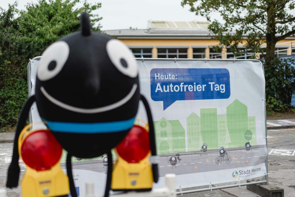 Das Maskottchen Edgar steht vor dem Banner "autofreier Tag".