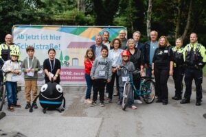 Schüler, Lehrer und Polizei stehen vor dem Schild der neuen Schulstraße.