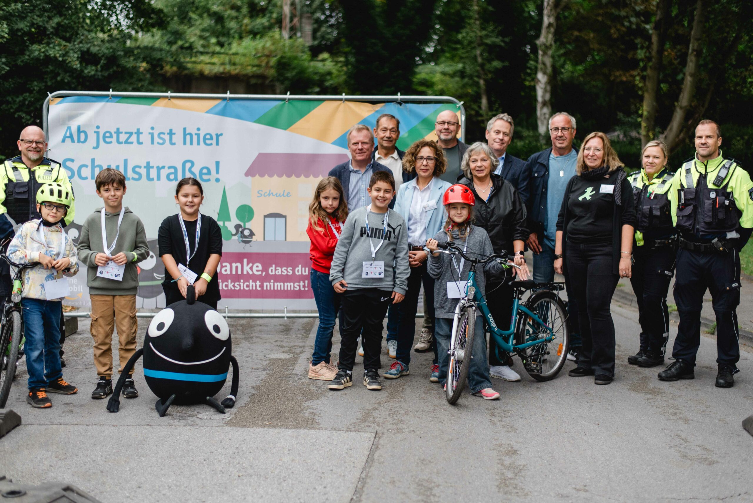Schüler, Lehrer und Polizei stehen vor dem Schild der neuen Schulstraße.